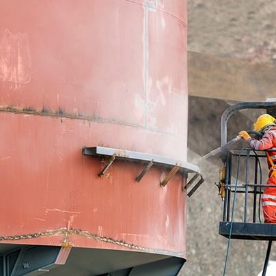 worker sandblasting the exterior of a steel tank