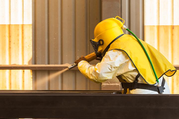 worker uses sand blasting process to clean steel surface