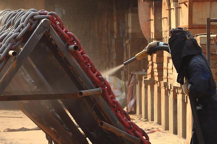 worker using abrasive blasting to clean large chains