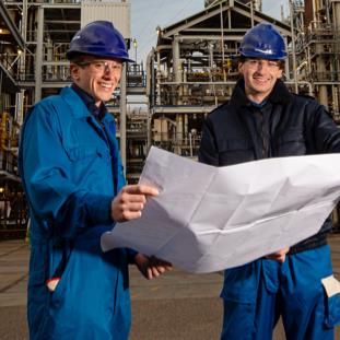 Two employees in hardhats looking at a project plan