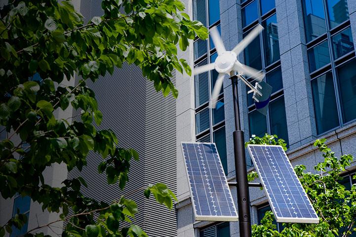 Post with wind turbines, over a solar panel in front of a building