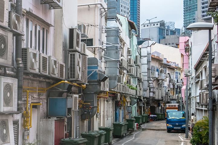crowded narrow street with many fans and ac units mounted on wall exteriors