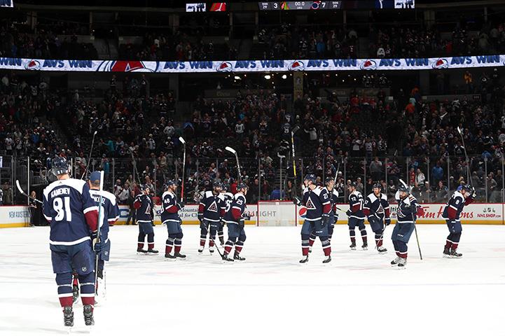 An image of a hockey team on ice raising there sticks celebrating.