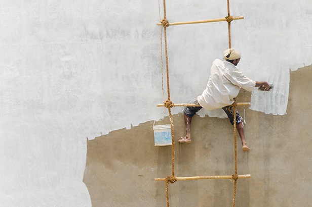 man sitting on rope and bamboo or rattan ladder painting a wall white