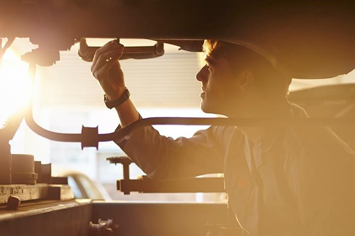 silhouette of mechanic working on underside of car