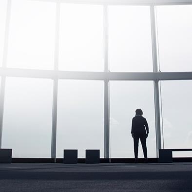 silhouetted person standing against a floor to ceiling bank of windows watching an airplane