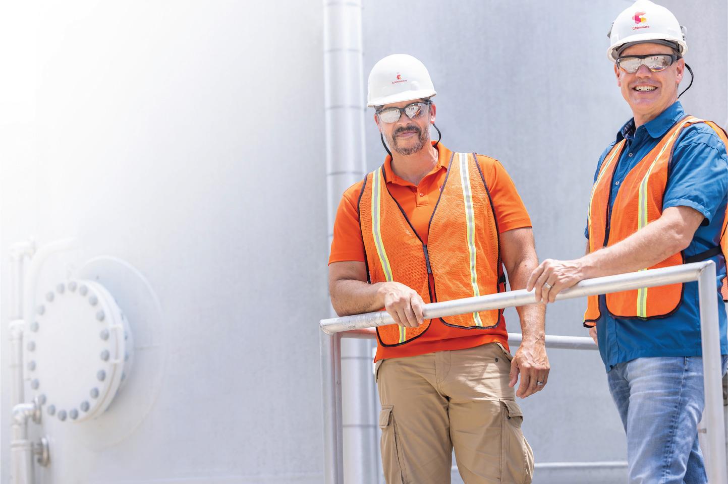 Two employees in hardhats, safety glasses, and high-visibility vests