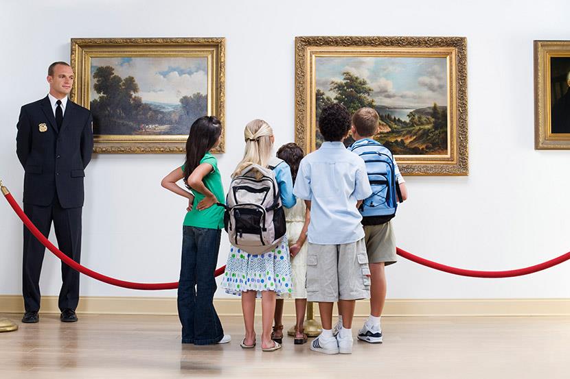 guard looking at students looking at paintings hung on an art museum wall 