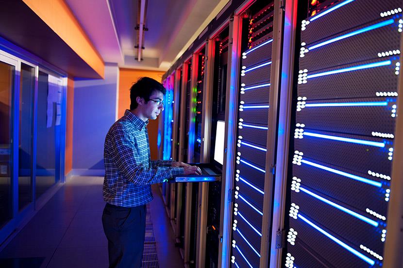 man typing on keyboard in datacenter room with wall of servers
