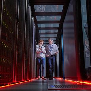 man and woman walking and talking together in a server room that has red floor lights