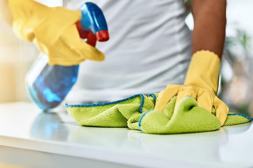 person wearing yellow gloves spritzing cleaning bottle and wiping counter clean with green cloth