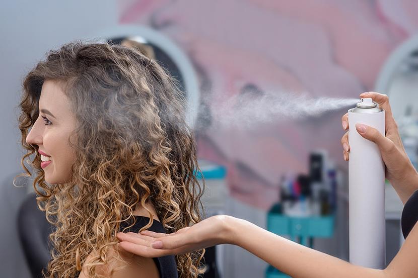 stylist spraying product on womans long hair at a salon 