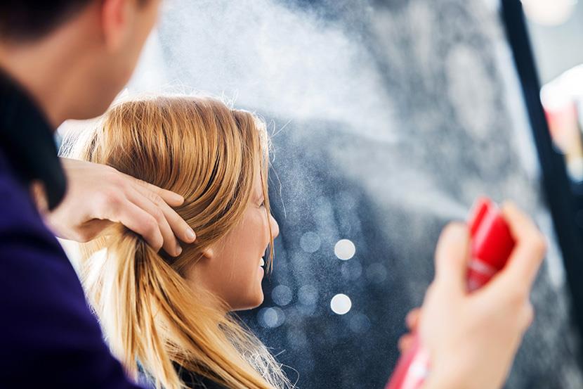 woman in chair at salon person spraying aerosol on hair 