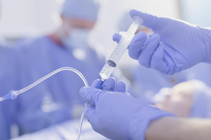 person wearing blue gloves holding syringe and injecting medicine into plastic tubing